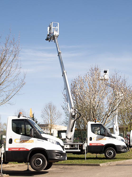 Two white bucket trucks with long articulated booms raised, parked on a street under a clear blue sky.