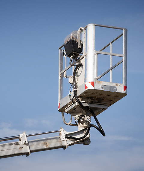 Aerial work platform bucket extended on a hydraulic arm against a blue sky.